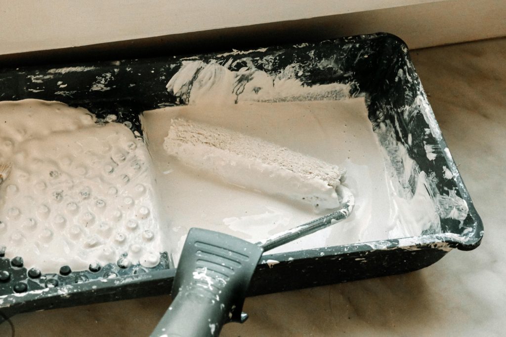 A picture of a painter's tray with white paint in it with a used painting roller.