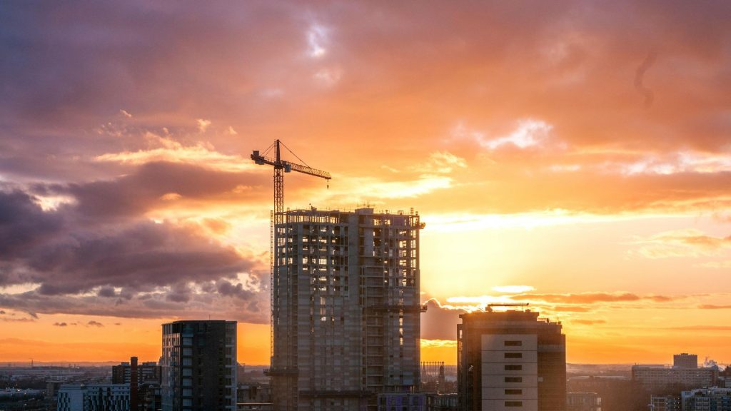 High-rise building under construction with tower crane at sunset over an urban skyline.