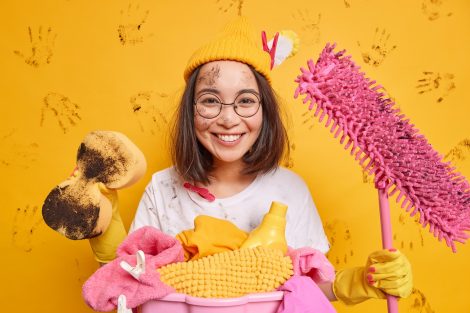 A picture depicting spring cleaning and decluttering with a smiling woman cleaning with a mess with cleaning supplies
