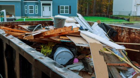 A picture of a full dumpster outside of a home filled with home renovation materials.